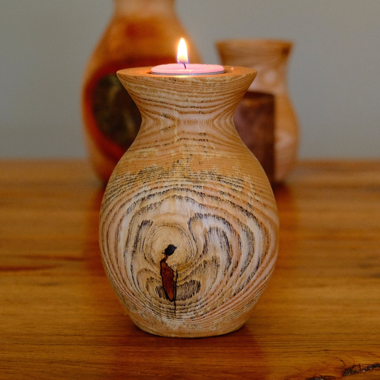 Wooden candle holder with a lit candle on a wooden surface